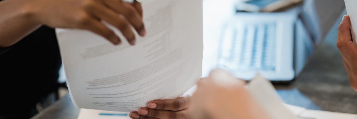 Mãos trocando documentos sobre a mesa de reunião